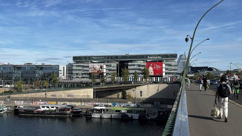 Façade du siège de France Télévisions à Paris, avec le logo france.tv, vue depuis un pont au bord de la Seine