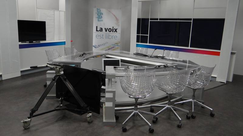 Un plateau de télévision vide avec ses fauteuils transparents, une caméra sur pied et un mur d'écrans