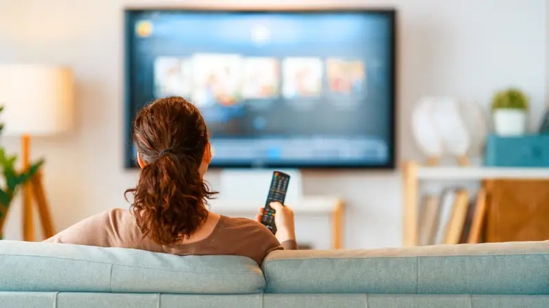 Une téléspectatrice devant sa télévision, télécommande en main, illustration des audiences TV