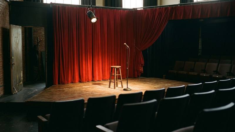 Petite scène de théâtre vide, rideau rouge à moitié tiré et projecteur allumé sur un tabouret, photo d'illustration sans personne identifiable
