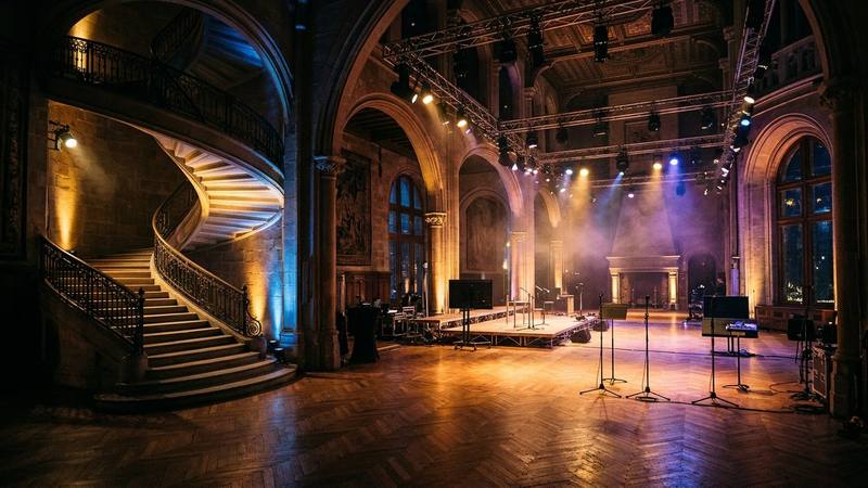 Grande salle d'un château illuminée la nuit avant un direct de télévision, projecteurs et escalier scénique, aucun texte ni personne identifiable, photo d'illustration