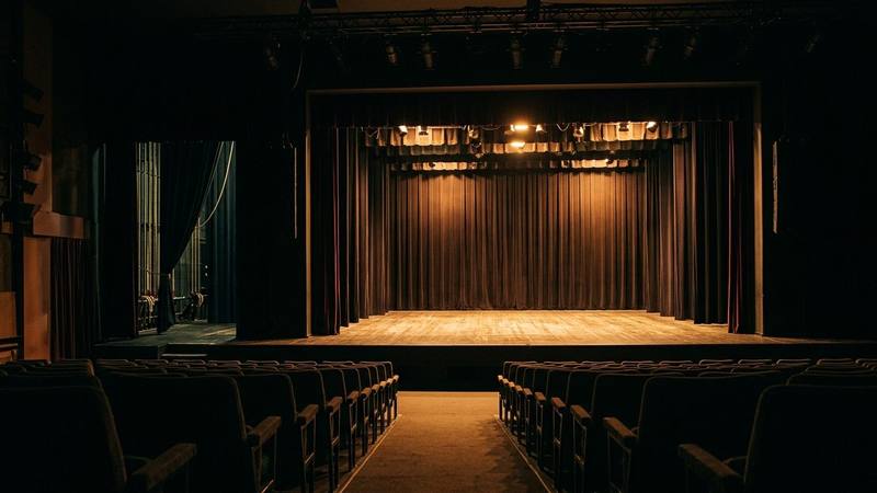 Petite scène de spectacle vide aux rideaux sombres, projecteurs allumés et coulisses visibles sur le côté, photo d'illustration sans lien direct avec la Star Academy