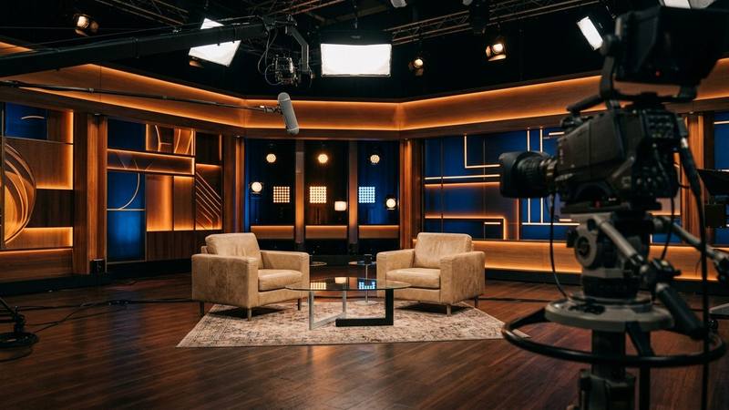 Plateau de talk-show de télévision aux lumières chaudes, deux fauteuils face à face autour d'une table basse, photo d'illustration sans personne identifiable